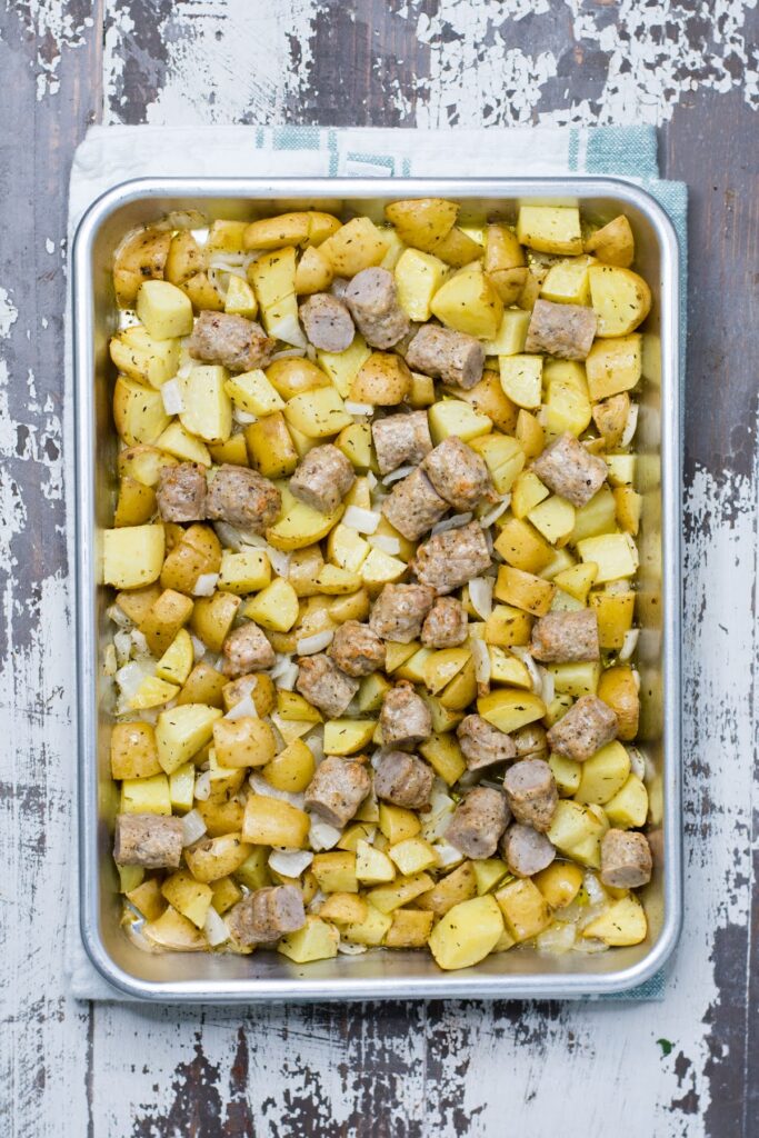 Seasoned potatoes, tender onions, and hearty sausage make this recipe for Baked Breakfast Potatoes with Sausage is a true crowd-pleaser. Sausage pieces added to sheet pan of potatoes and onions.
