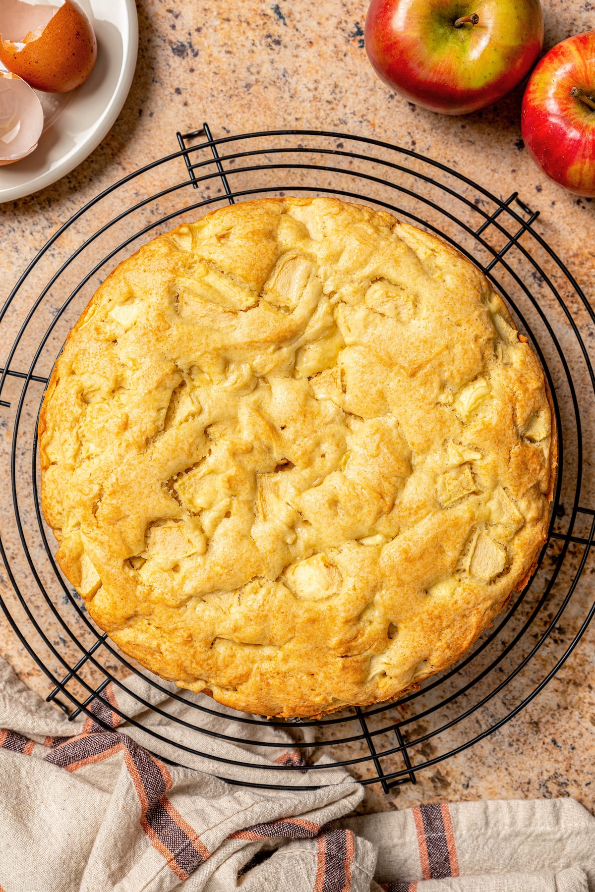 This fluffy apple cake recipe dusted with powdered sugar is an easy fall-flavored dessert once the leaves start falling. Whole, freshly-baked cake on a cooling rack.