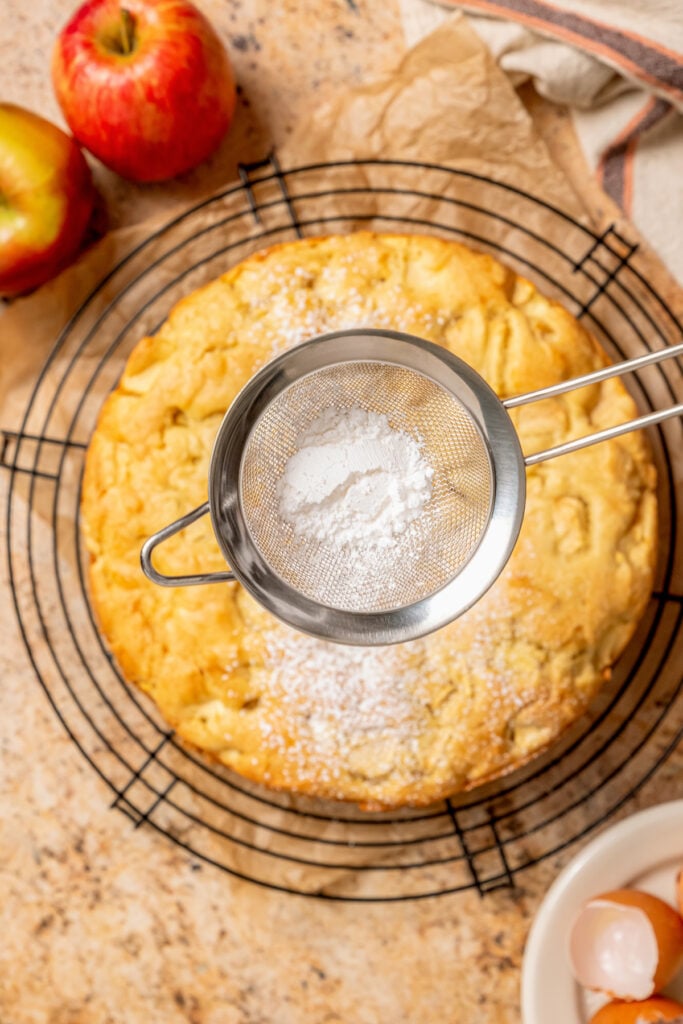 This fluffy apple cake recipe dusted with powdered sugar is an easy fall-flavored dessert once the leaves start falling. Dusting the cake with powdered sugar.