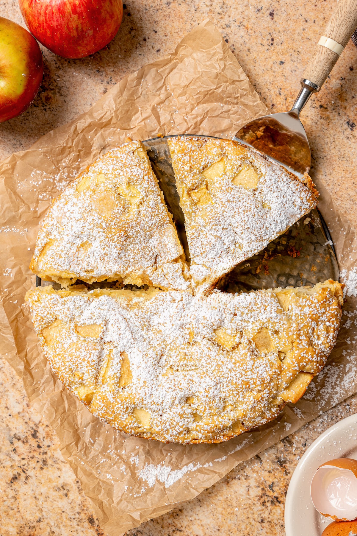 This fluffy apple cake recipe dusted with powdered sugar is an easy fall-flavored dessert once the leaves start falling. Grabbing a slice of fruity cake with powdered sugar on top.