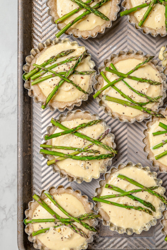 This asparagus tartlets recipe with zesty parmesan custard and buttery crust is an easy way to impress guests for brunch. Adding filling and asparagus to the tart shells.