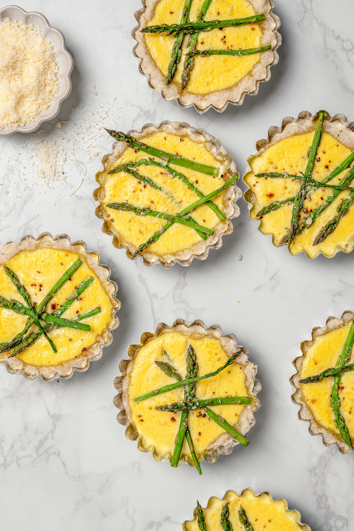 This asparagus tartlets recipe with zesty parmesan custard and buttery crust is an easy way to impress guests for brunch. Freshly-baked lemon asparagus tartlets on the counter.