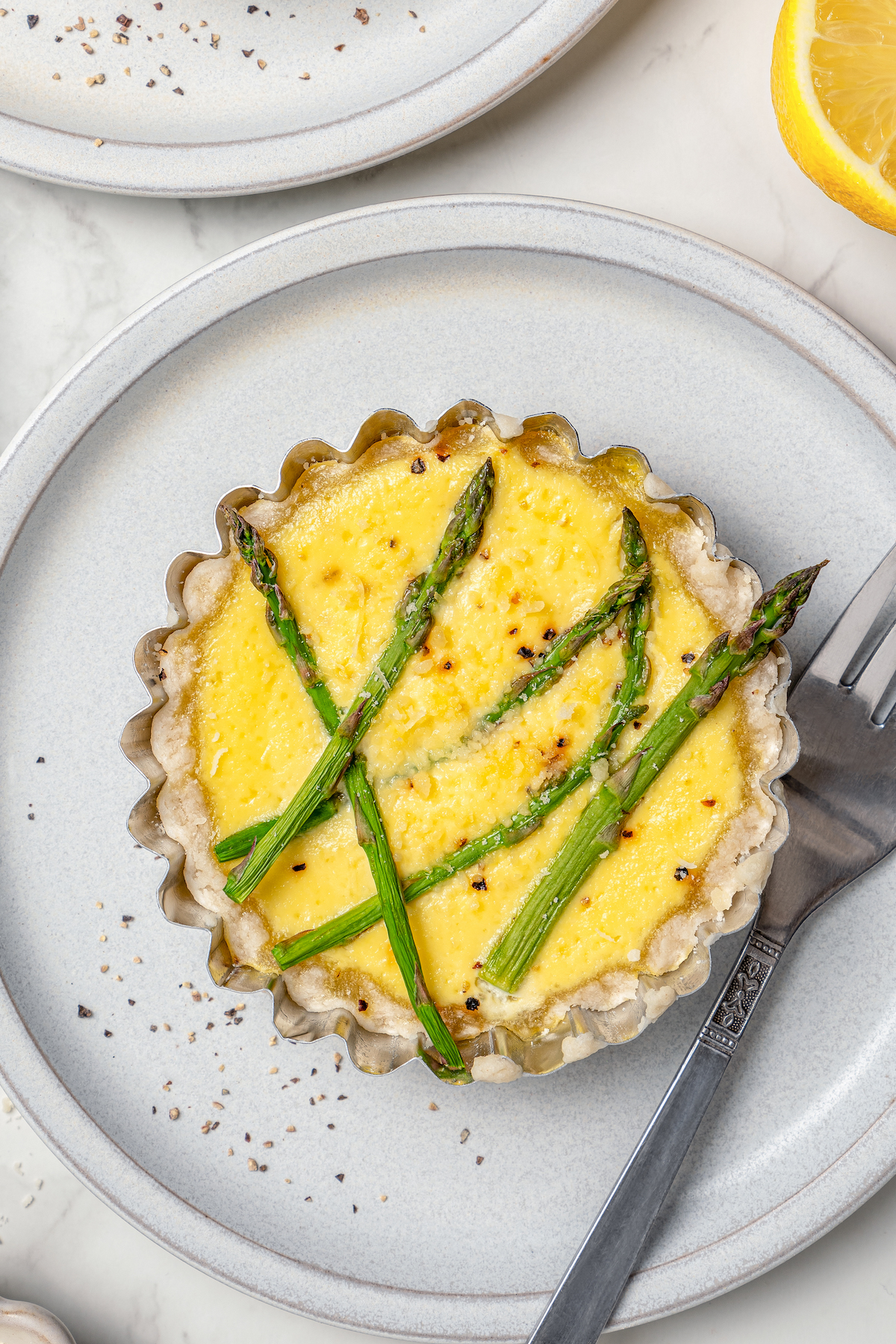 This asparagus tartlets recipe with zesty parmesan custard and buttery crust is an easy way to impress guests for brunch. Overhead photo of a creamy tart on a serving plate.