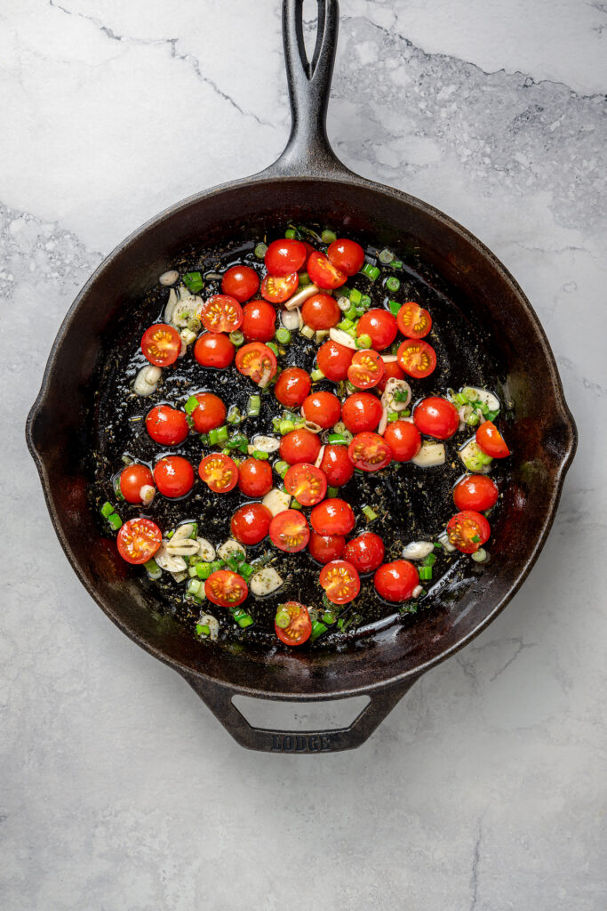 Baked Shrimp with Tomato and Feta is an easy, gluten free, healthy dinner that is made in one skillet and ready in less than 30 minutes. Tomatoes and aromatics cooking in a skillet.