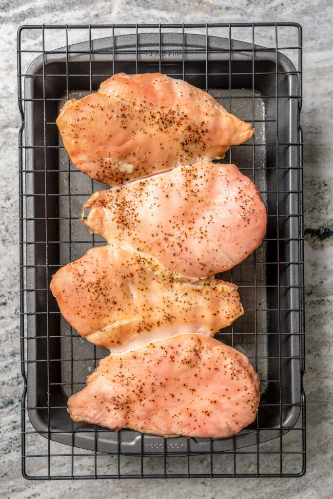 This juicy, grilled BBQ chicken recipe is coated in your favorite barbecue sauce for a sweet-and-savory cookout dinner. Placing the seasoned chicken breasts on the cooking rack over the pan.