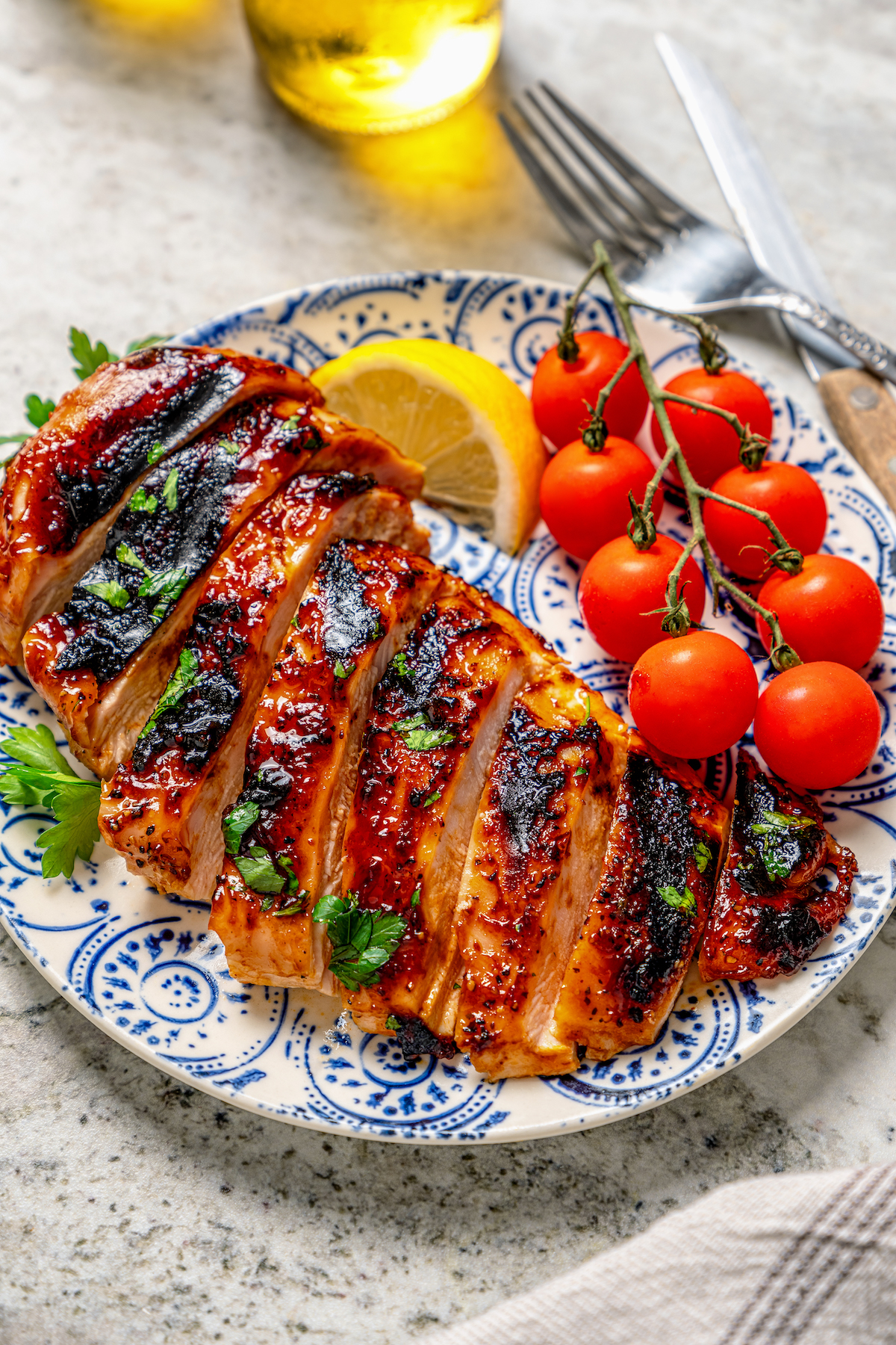 This juicy, grilled BBQ chicken recipe is coated in your favorite barbecue sauce for a sweet-and-savory cookout dinner. Freshly-grilled BBQ chicken recipe with cherry tomatoes and a lemon wedge on the side.