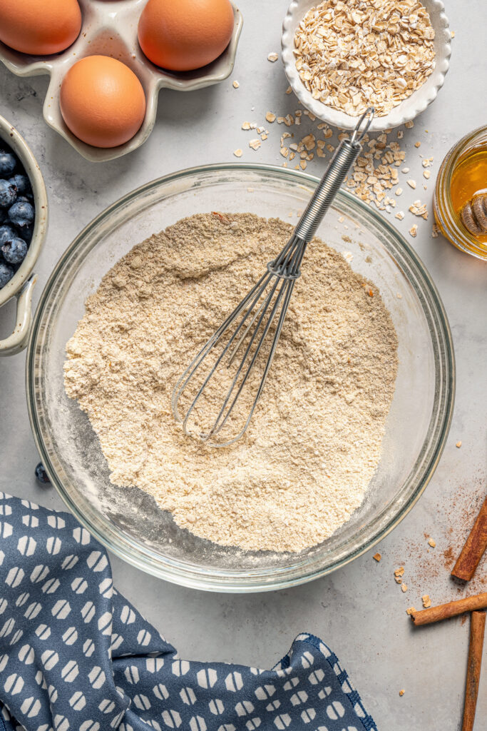 This naturally-sweetened blueberry protein muffins recipe with cinnamon and orange zest is a great on-the-go breakfast. Whisking the dry ingredients in a bowl.