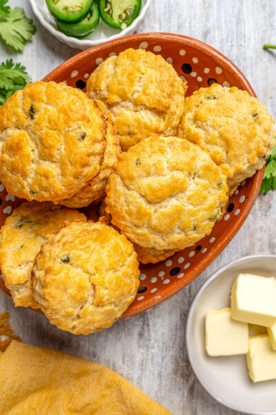 Homemade cheddar biscuits next to a dish of butter and one of jalapenos.