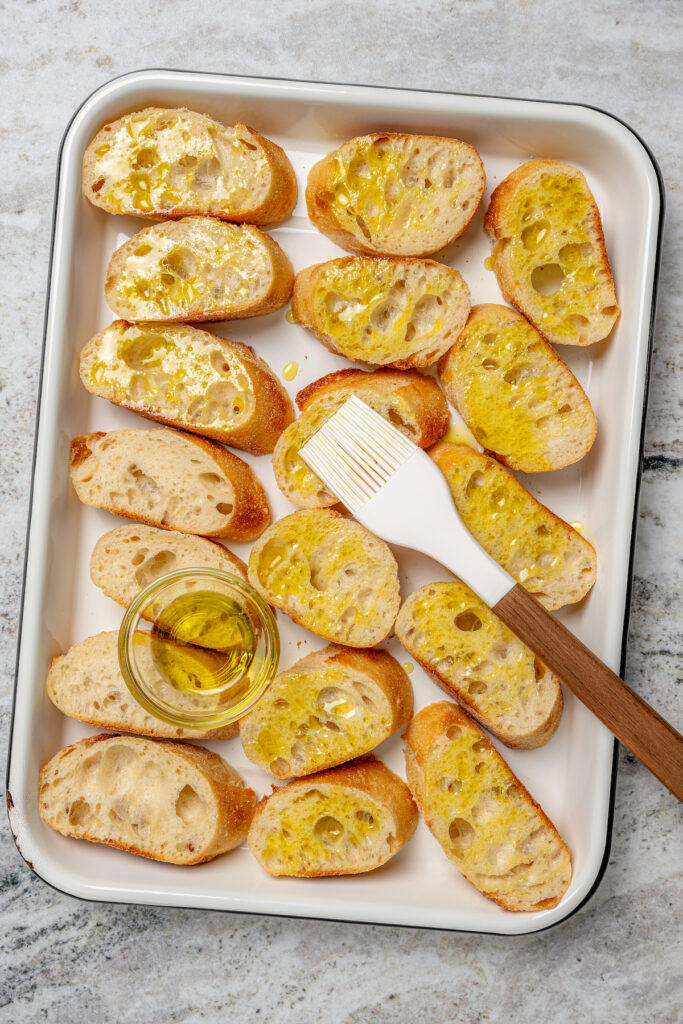 This zesty chickpea bruschetta recipe with herby pesto and salty olives on toasty bread is a 20-minute summer appetizer. Brushing the bread with olive oil.