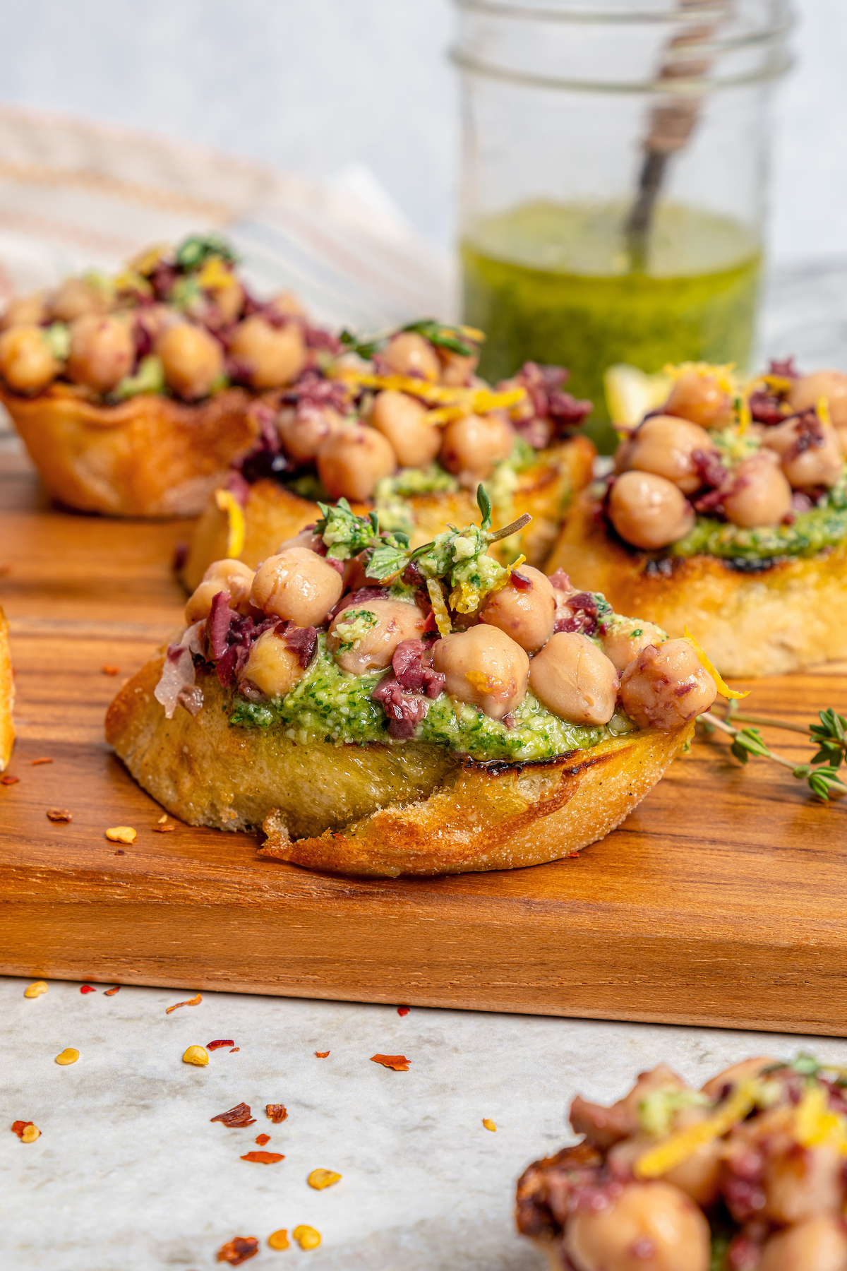 This zesty chickpea bruschetta recipe with herby pesto and salty olives on toasty bread is a 20-minute summer appetizer. Close-up of chickpea bruschetta with lemon zest and fresh thyme on top.