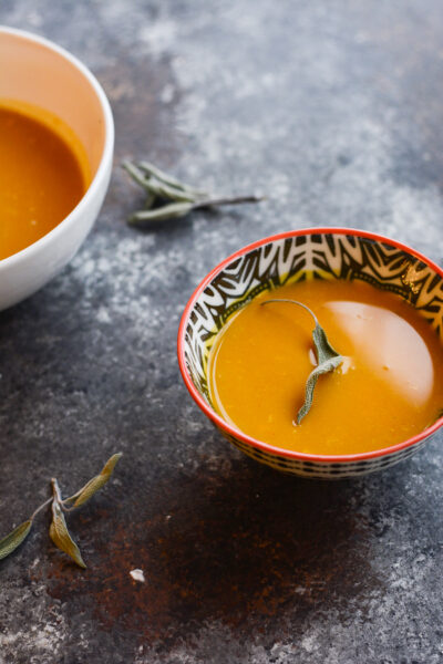 A bowl of pumpkin soup on a countertop with a second bowl beside it