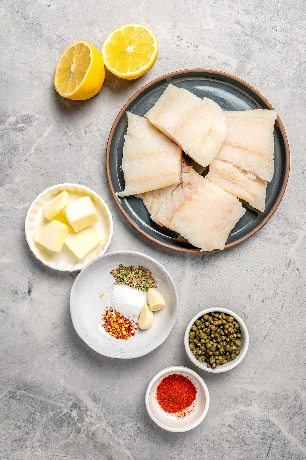 You'll crave the light, fresh flavors of this easy Baked Cod Recipe. Simple prep, perfect texture, and zingy flavor - what could be better? Ingredients for a simple baked cod recipe, measured and arranged on a table.