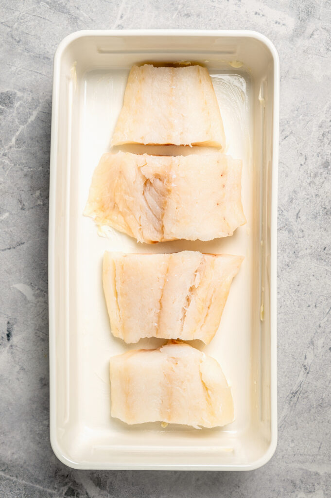 You'll crave the light, fresh flavors of this easy Baked Cod Recipe. Simple prep, perfect texture, and zingy flavor - what could be better? Pieces of fish laid in a row in a baking dish.