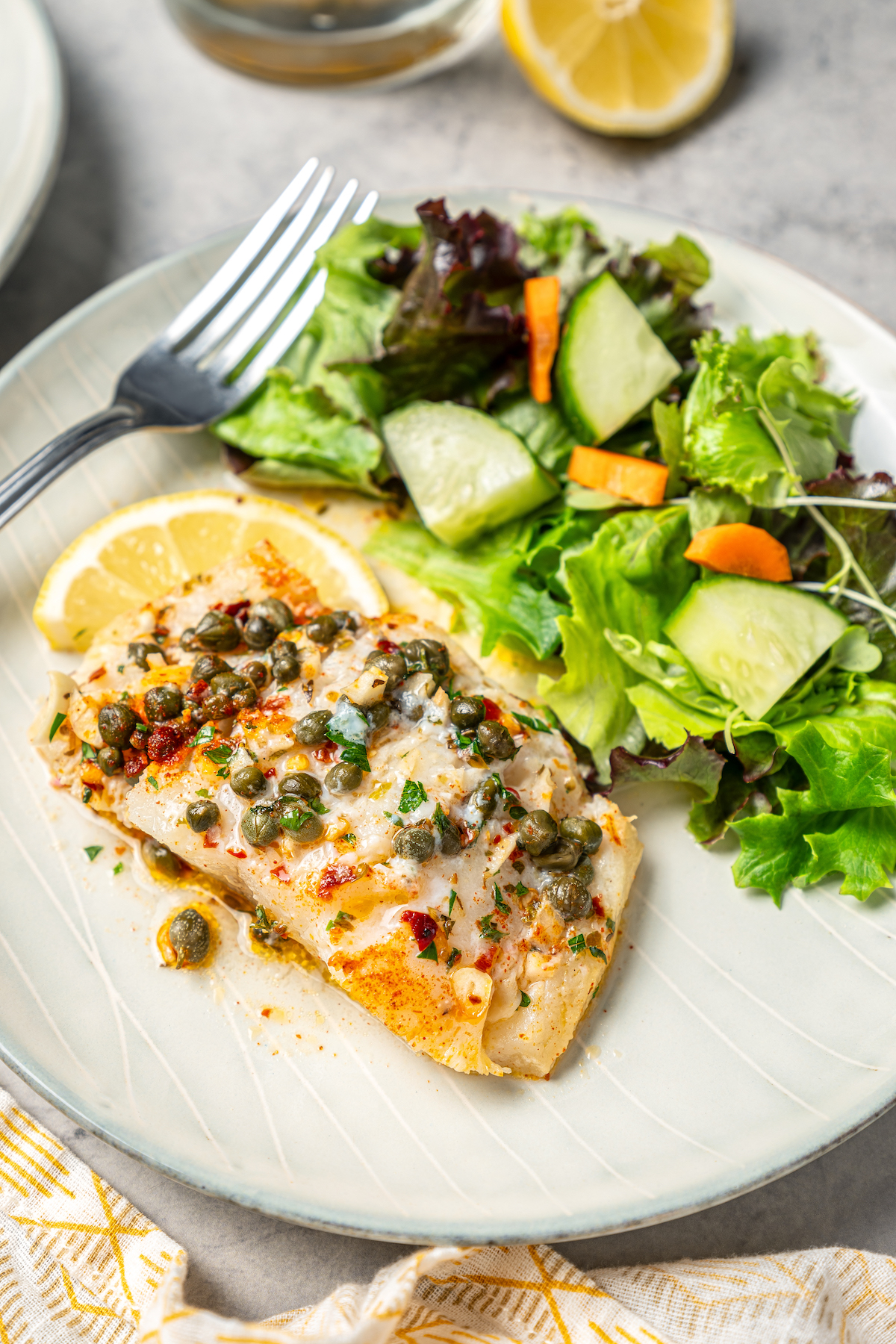 You'll crave the light, fresh flavors of this easy Baked Cod Recipe. Simple prep, perfect texture, and zingy flavor - what could be better? A piece of baked cod on a dinner plate with salad.