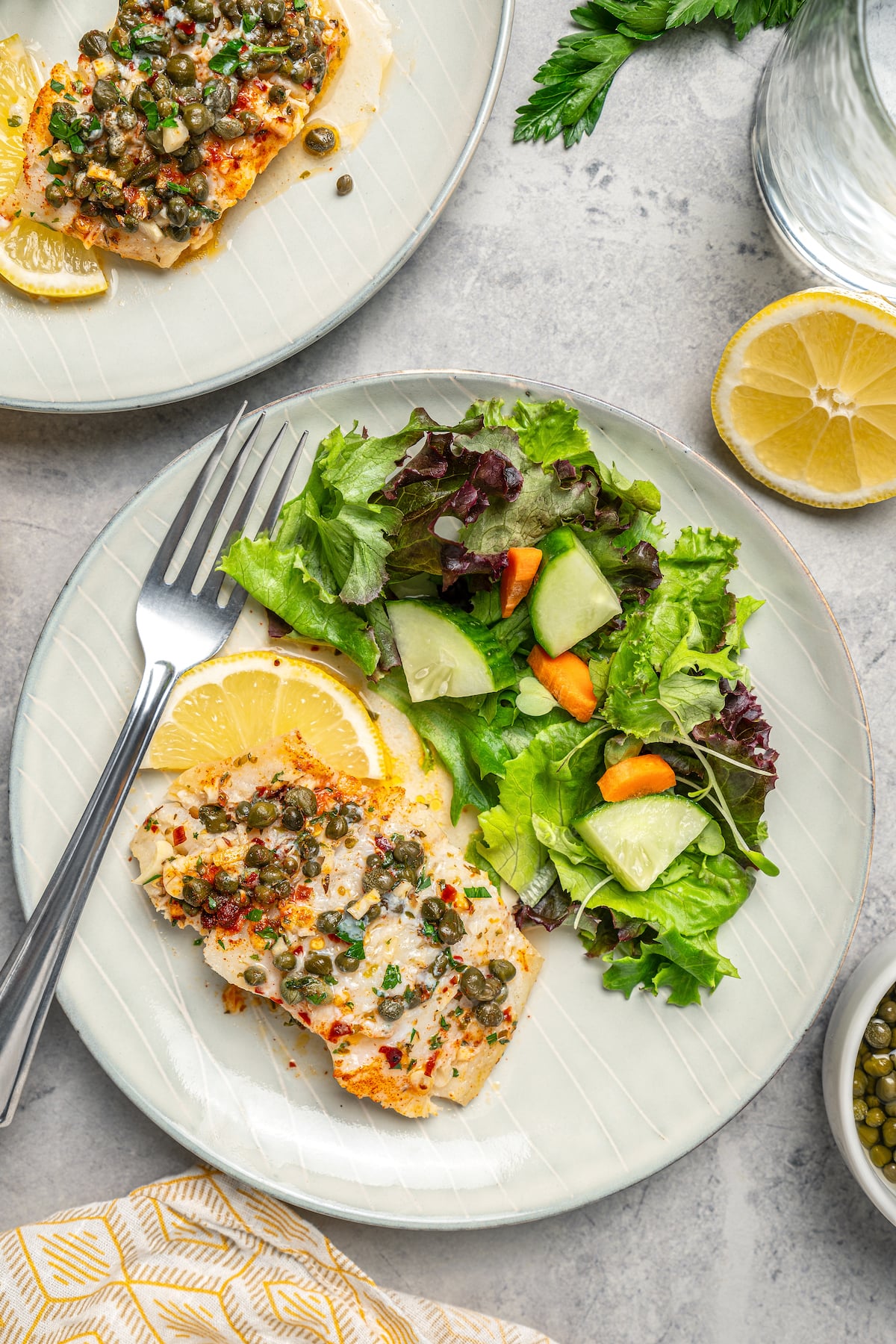 You'll crave the light, fresh flavors of this easy Baked Cod Recipe. Simple prep, perfect texture, and zingy flavor - what could be better? Two servings of fish with salad and lemon slices.