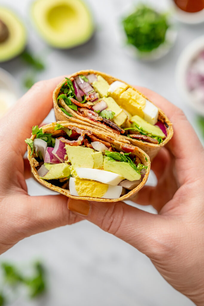 This Egg and Avocado Breakfast Wrap is low-carb and loaded with protein. Healthy, clean, and delicious, it’s a quick breakfast you'll crave! Holding a halved breakfast wrap toward the camera.