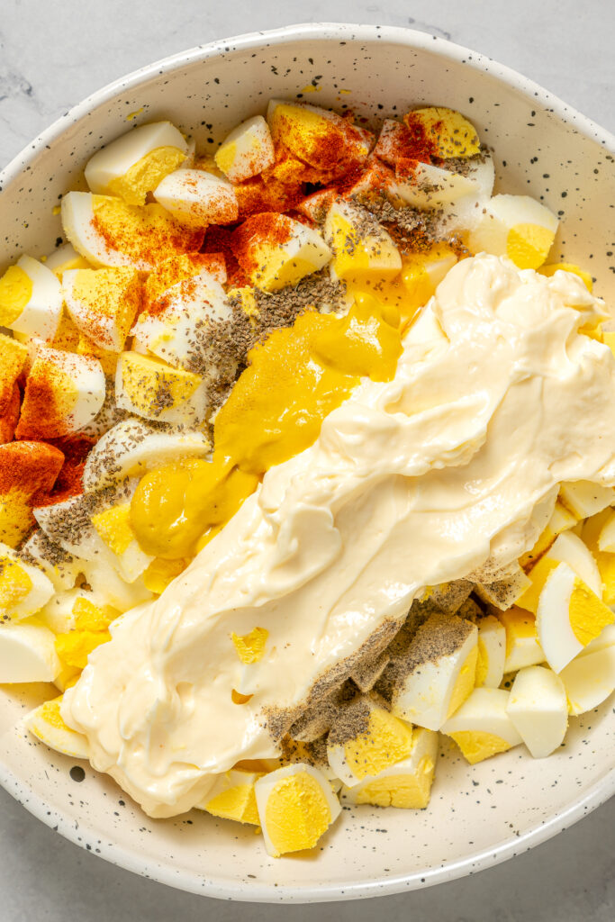 This Healthy Egg Salad is a simple, tasty recipe that’s packed with protein and easy to prepare. A scrumptious lunch or midday snack! Cubed hard-boiled eggs, mustard, mayonnaise, and other ingredients in a mixing bowl.