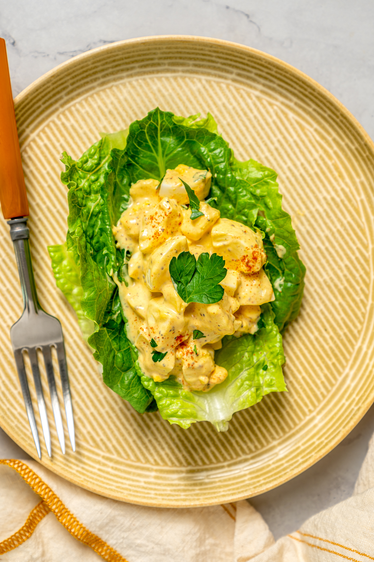 This Healthy Egg Salad is a simple, tasty recipe that’s packed with protein and easy to prepare. A scrumptious lunch or midday snack! A serving of the salad on a romaine lettuce leaf, served on a small bamboo plate.