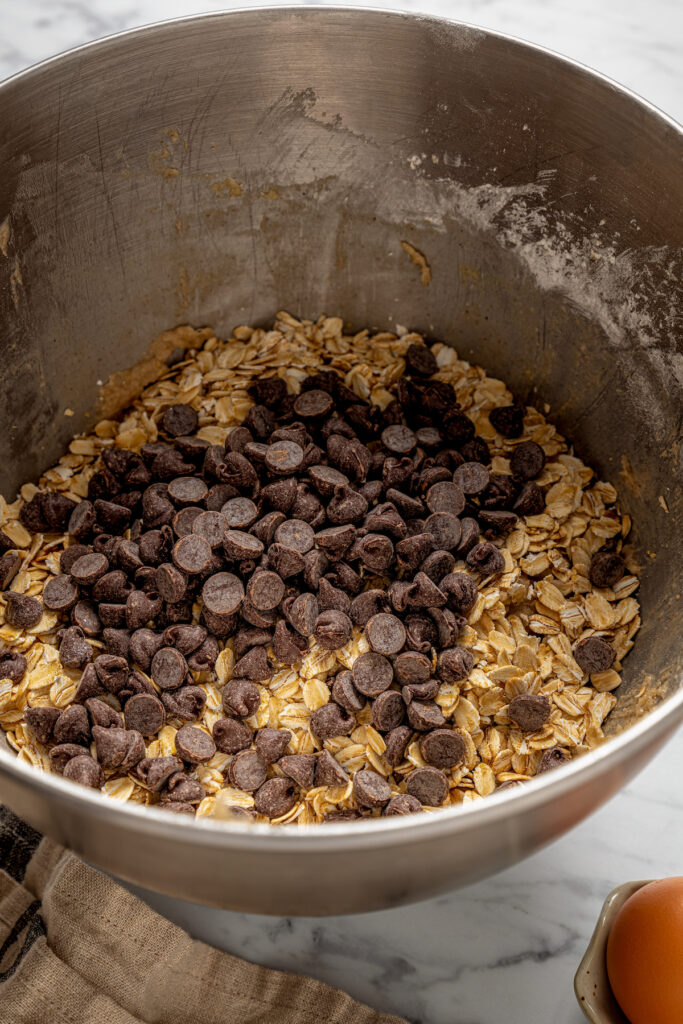 This banana oatmeal chocolate chip cookies recipe is warmly spiced with cinnamon and cardamom for a comforting, freshly baked treat. Folding the chocolate chips into the dough.