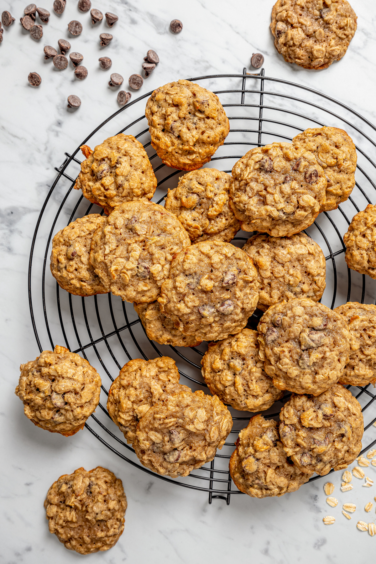 This banana oatmeal chocolate chip cookies recipe is warmly spiced with cinnamon and cardamom for a comforting, freshly baked treat. Lots of banana oatmeal chocolate chip cookies on a cooling rack.