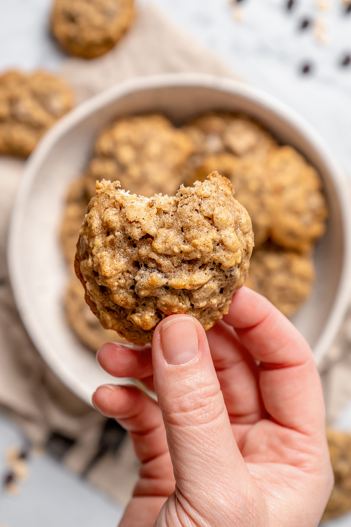 This banana oatmeal chocolate chip cookies recipe is warmly spiced with cinnamon and cardamom for a comforting, freshly baked treat. Close-up of a bitten oatmeal chocolate chip cookies.