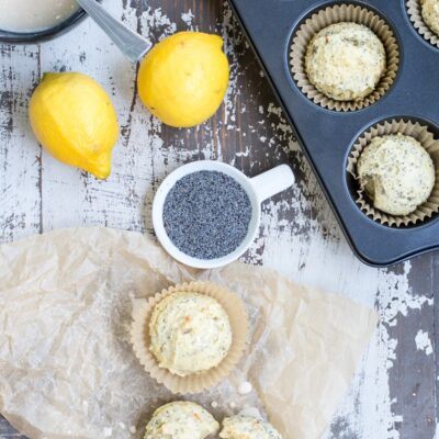 Overhead shot of a table with a muffin tin, lemons, glaze, and other items. Two muffins are nearby on the counter.