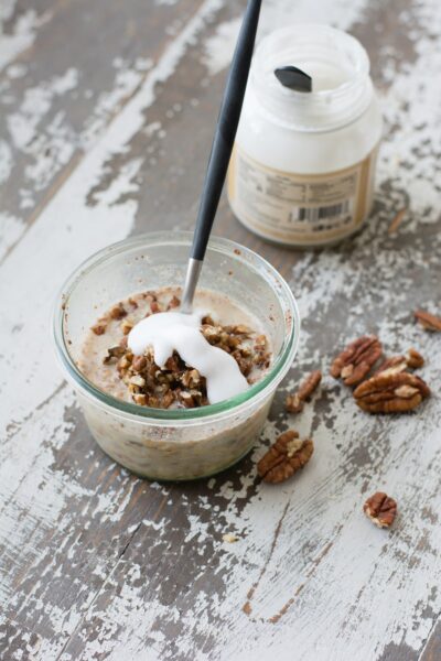A small glass dish of overnight oatmeal with pecan topping and yogurt.