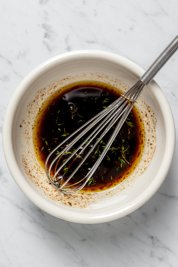 Grilled Asparagus with Onion recipe is topped with simple vinaigrette, blue cheese, black Mission figs, and toasted pine nuts. So flavorful! Vinaigrette in a bowl with a whisk.