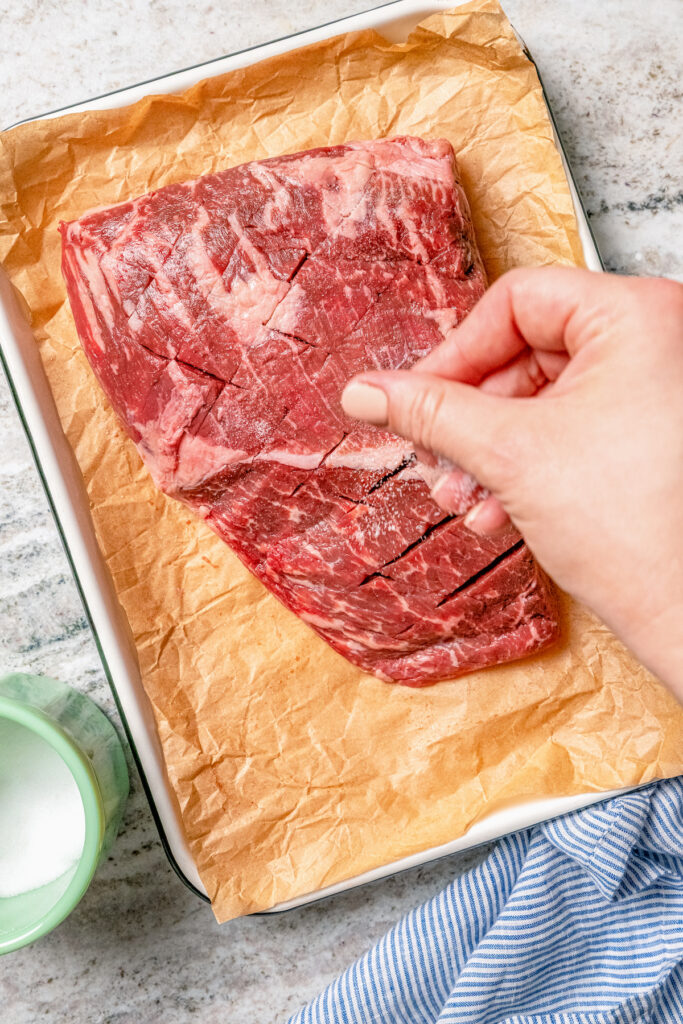 This juicy grilled tri tip recipe with homemade Sicilian herb sauce is an easy dinner for your next summer cookout. Sprinkling salt over the scored beef roast.