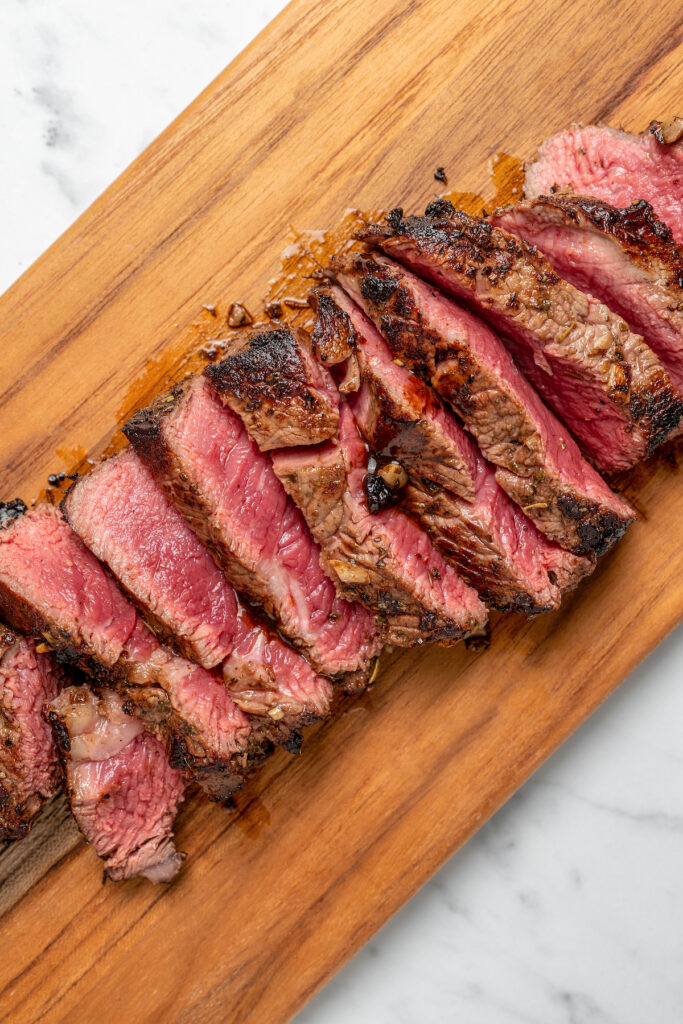 This Pan Seared Steak Recipe with Roasted Vegetables is hearty, filling, and easy to make. A crazy-good marinade brings it all together! Sliced steak on a cutting board.