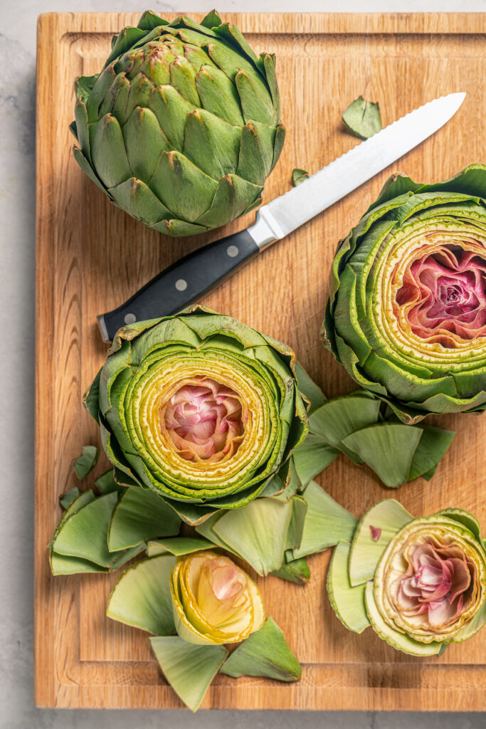 This tender Instant Pot artichokes recipe with hints of tangy lemon, garlic, and fresh herbs will be your go-to holiday side dish. Cutting off the top 1/3 of the artichokes with a knife.