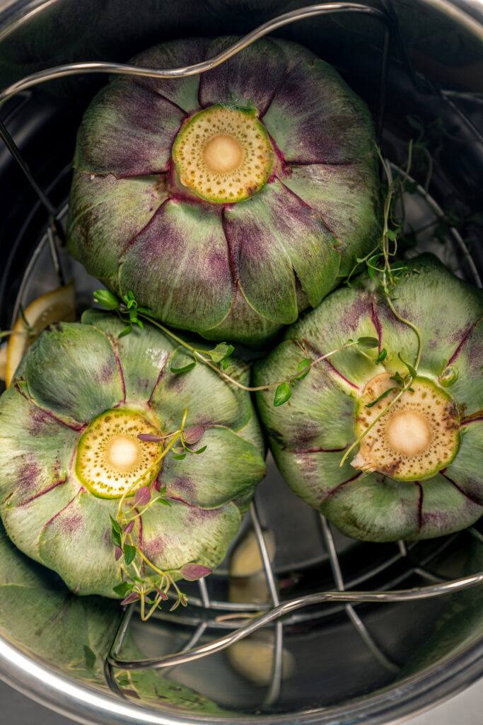 This tender Instant Pot artichokes recipe with hints of tangy lemon, garlic, and fresh herbs will be your go-to holiday side dish. Placing the artichokes in the Instant Pot.