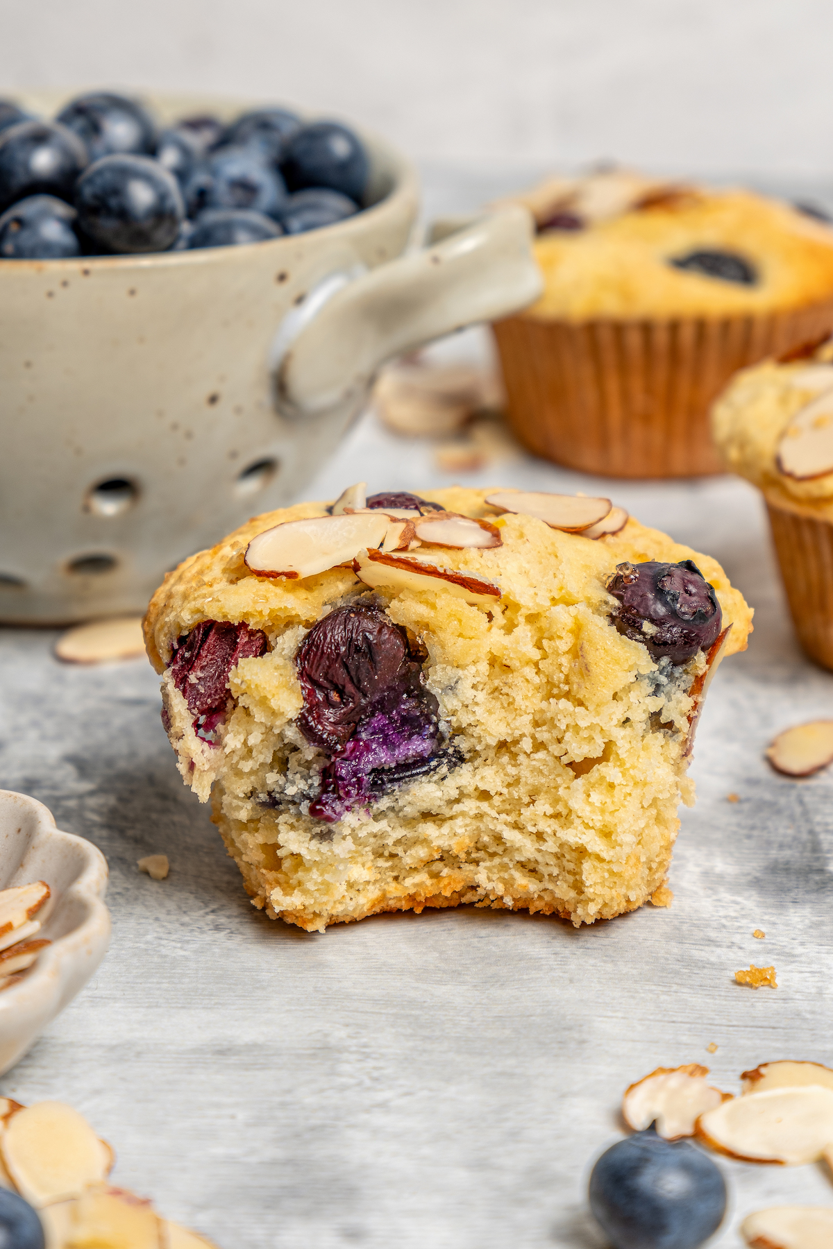 These lemon-blueberry ricotta muffins with crunchy almonds are an easy 20-minute baked treat. They're so light and fluffy you'd never guess they're gluten-free! Add shredded coconut for extra fruity vibes. Halved, fluffy ricotta muffin close-up.