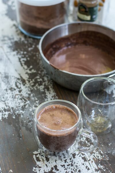 A warm maca latte next to a saucepan of the mixture and an extra empty glass.