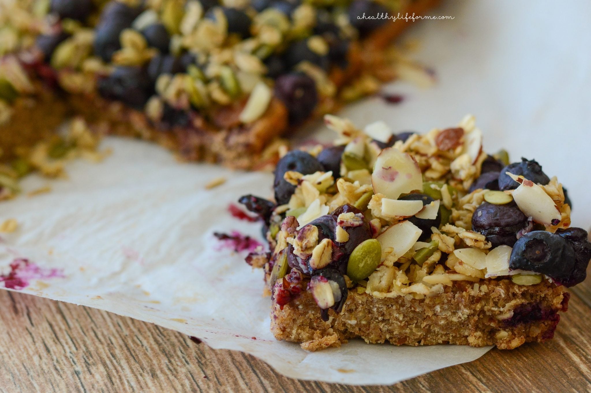 These easy oatmeal breakfast bars with sweet blueberries and pumpkin seeds are a quick high-protein treat for busy mornings. Close-up of one breakfast bar with toppings.