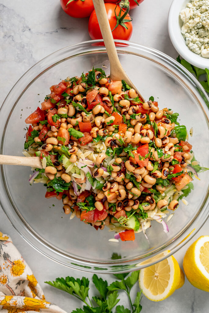 This orzo and black eyed pea salad recipe with crunchy veggies and two homemade vinaigrettes is a refreshing summer side. Mixing the orzo, black-eyed pea mixture, cucumber, onions, and lemon vinaigrette.