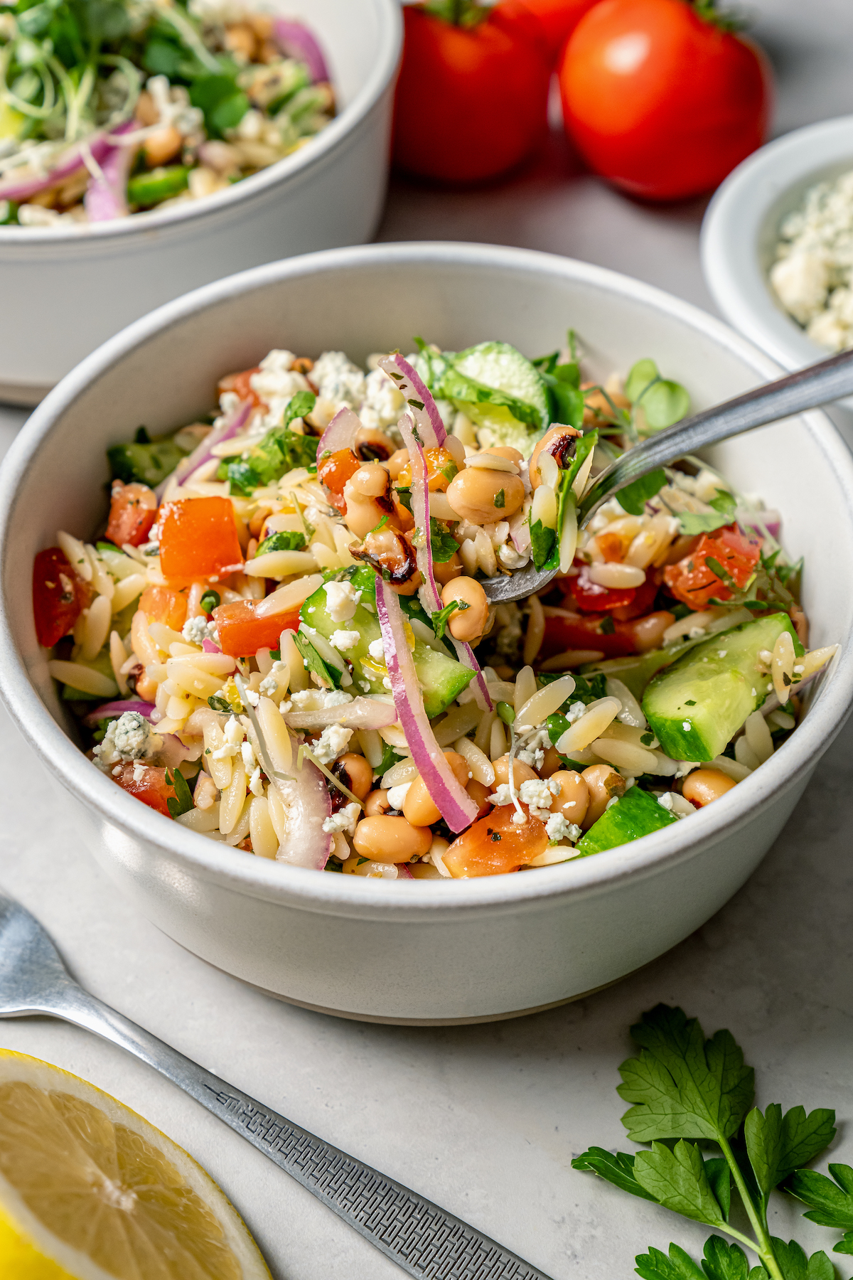 This orzo and black eyed pea salad recipe with crunchy veggies and two homemade vinaigrettes is a refreshing summer side. Close-up of black eyed pea salad with microgreens, vinaigrette, and blue cheese.