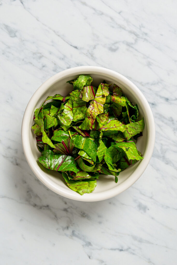This vibrant Orzo Salad is made with beets, pasta, toasted pine nuts, and blue cheese - a wholesome side dish that everyone will love. Sliced, washed beet greens in a bowl.