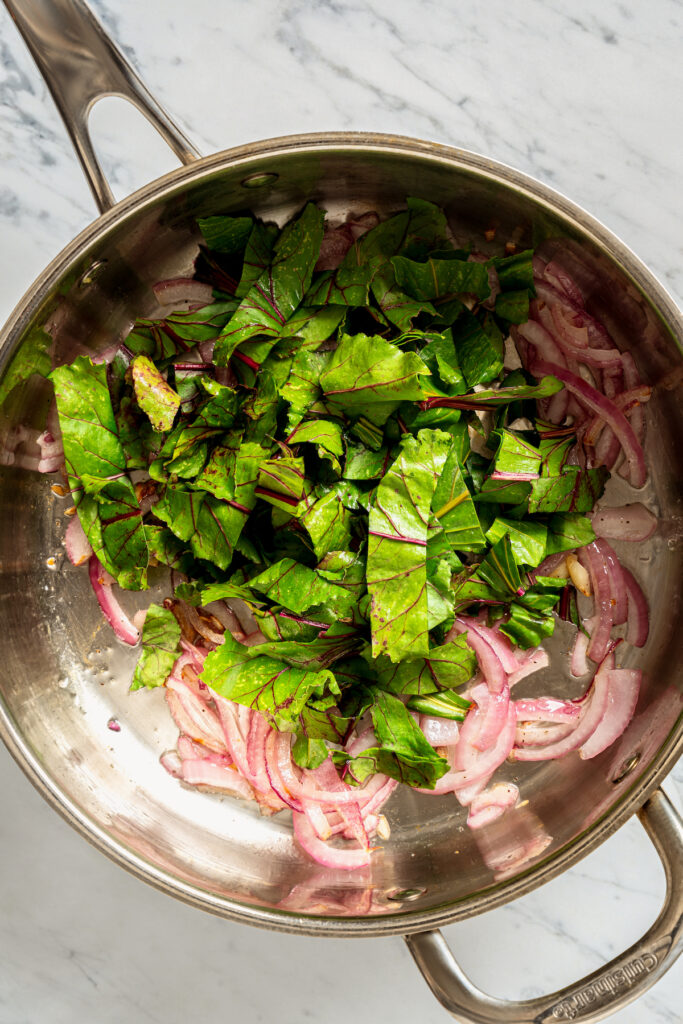 This vibrant Orzo Salad is made with beets, pasta, toasted pine nuts, and blue cheese - a wholesome side dish that everyone will love. Wilting beet greens in a pan.