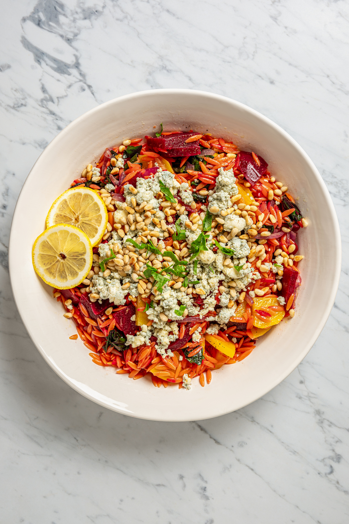 This vibrant Orzo Salad is made with beets, pasta, toasted pine nuts, and blue cheese - a wholesome side dish that everyone will love. A bowl of beet and orzo salad topped with blue cheese.