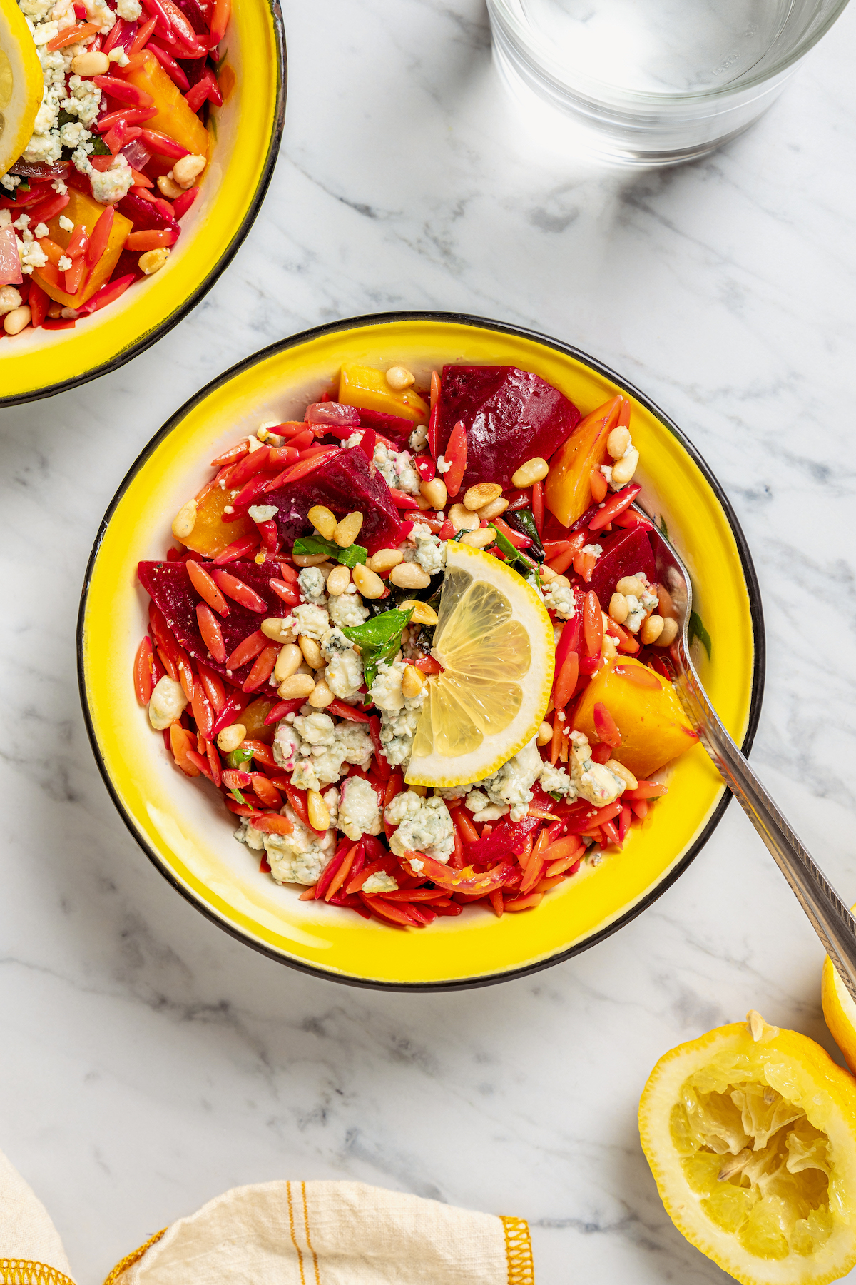 This vibrant Orzo Salad is made with beets, pasta, toasted pine nuts, and blue cheese - a wholesome side dish that everyone will love. A serving of salad in a bright yellow bowl.