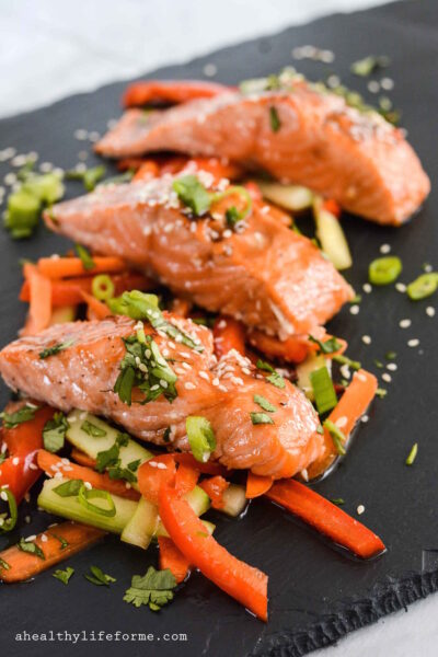 Close-up of flaky teriyaki salmon with seasoned veggies, sesame seeds, and green onions.