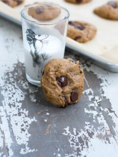 A protein cookie next to a glass of milk and a baking sheet of additional cookies.