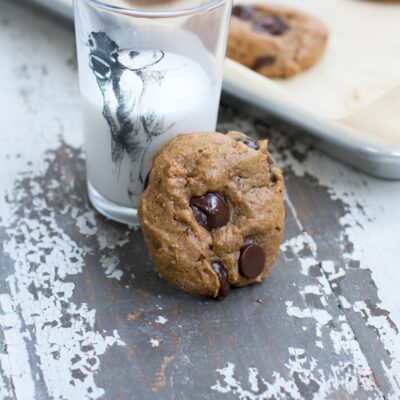 A protein cookie next to a glass of milk and a baking sheet of additional cookies.