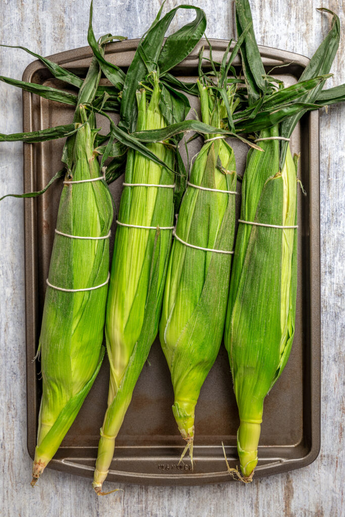 Sweet, fresh corn is a must-have in the summer, and this easy Grilled Corn is loaded with a unique nutty taste that you're sure to love! Ears of corn with the husks replaced and tied at the top with kitchen twine.