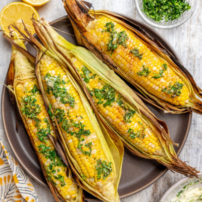 A plate of corn cooked in the husk, next to dishes of toppings.