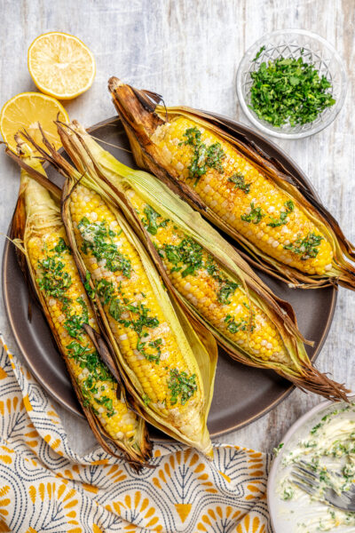 A plate of corn cooked in the husk, next to dishes of toppings.