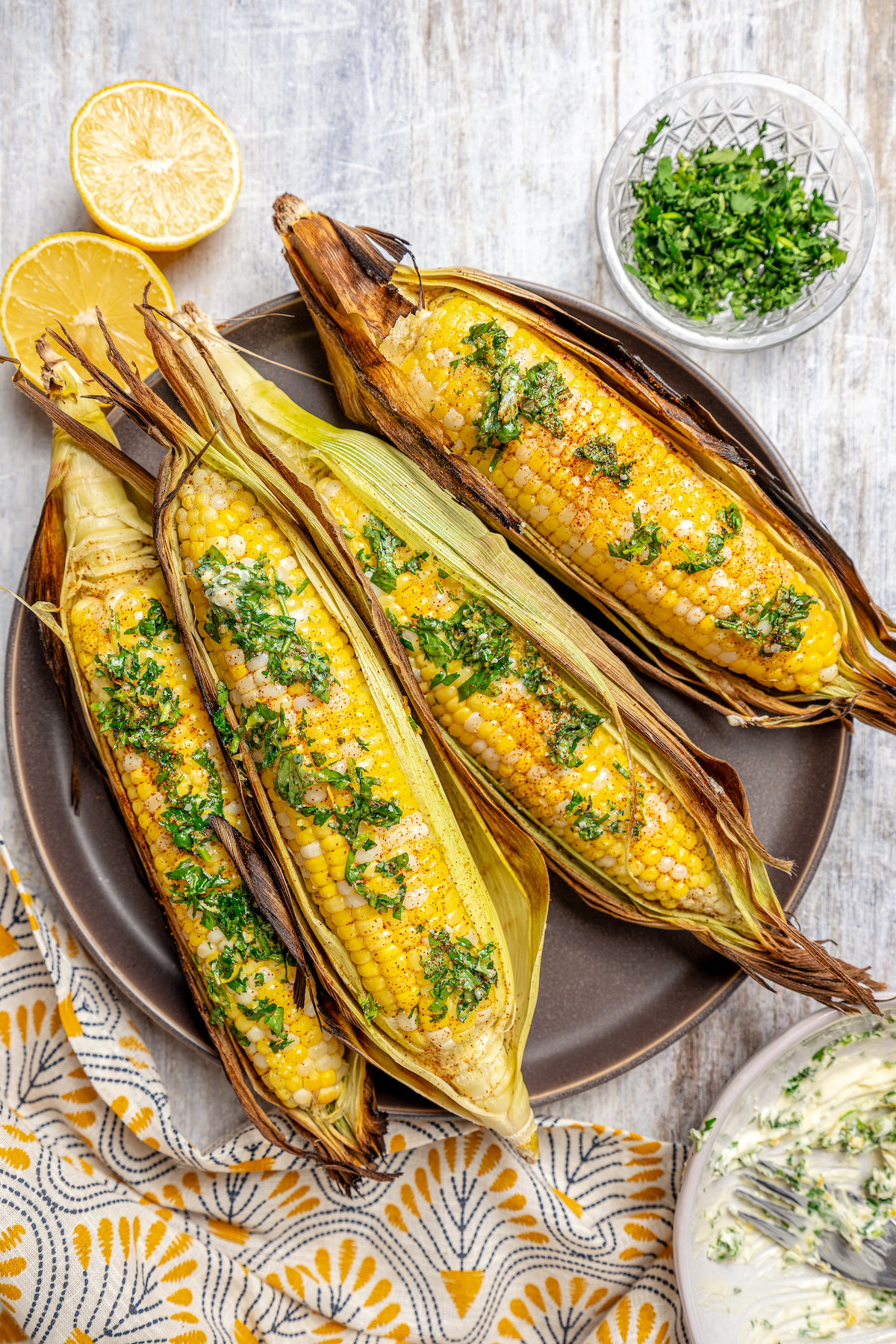 Sweet, fresh corn is a must-have in the summer, and this easy Grilled Corn is loaded with a unique nutty taste that you're sure to love! A plate of corn cooked in the husk, next to dishes of toppings.