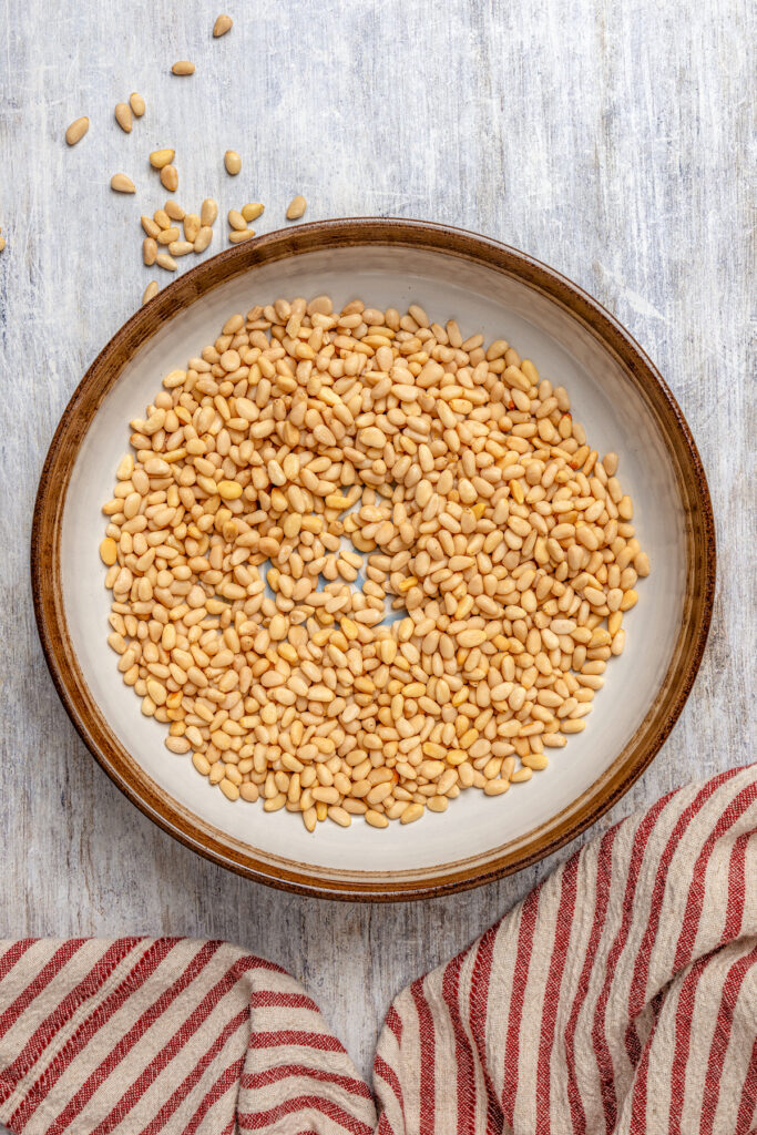 Italian Pignoli Cookies are crispy, chewy and almond-y, topped with rich, creamy pine nuts. They're sure to become a family favorite! Pine nuts in a shallow dish.