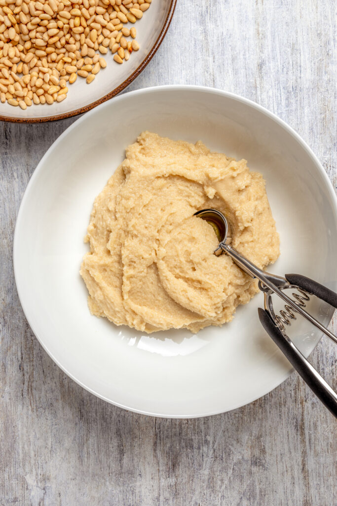 Italian Pignoli Cookies are crispy, chewy and almond-y, topped with rich, creamy pine nuts. They're sure to become a family favorite! Scooping dough with a cookie scoop.
